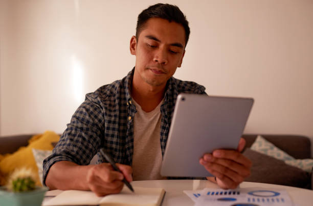 istock Shot of a handsome young man sitting alone and using a digital tablet to work from home 1323980769