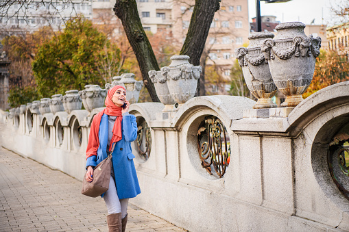A Woman of Muslim Ethnicity is Walking in a City Streets During an Autumn Day and Using a Mobile Phone for Communication.