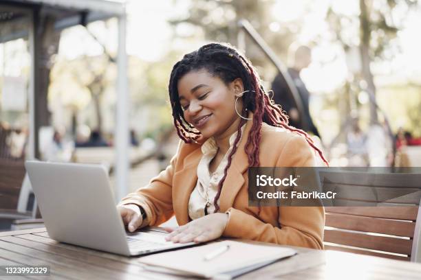 Young smiling african american woman sitting at the table in street cafe and using laptop
