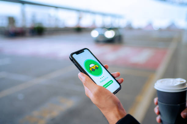 istock Chic young Asian man using mobile app device on smartphone to order a taxi pick up service by the urban road in downtown city street. Speedy and trustworthy service. Carsharing and business on the go themes 1323994548