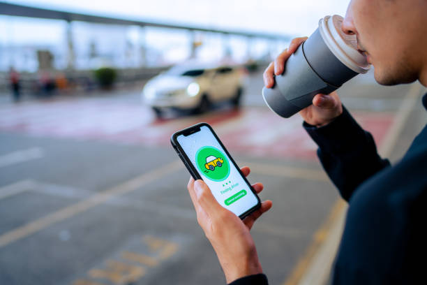 istock Chic young Asian man using mobile app device on smartphone to order a taxi pick up service by the urban road in downtown city street. Speedy and trustworthy service. Carsharing and business on the go themes 1323994552