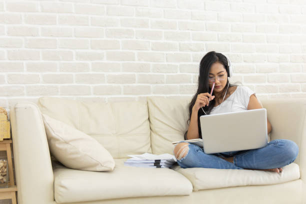 istock A young Asian woman working online from home.  She uses a headset video conference calling on laptop computer talk by webcam. She avoids the outbreak of coronavirus. The Internet is everything. 1324001087