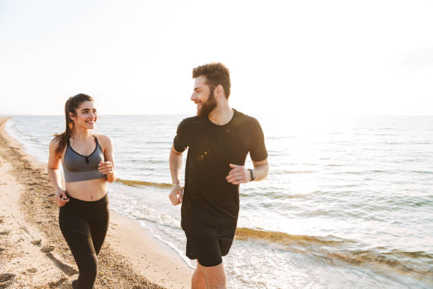 istock Cheerful young couple jogging together on a beach 1324003222