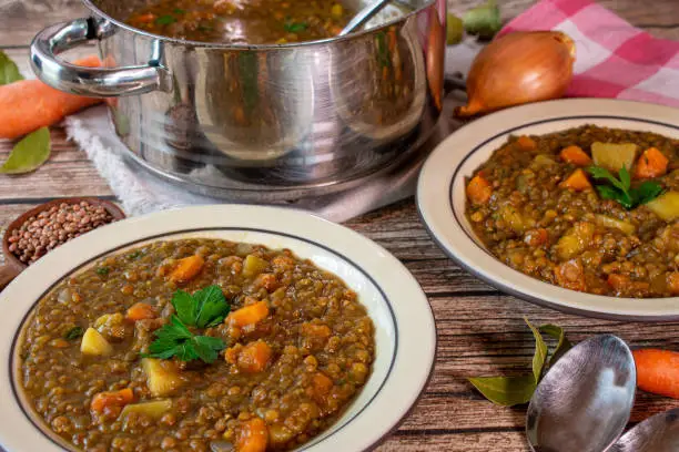 fresh cooked and homemade vegetarian and vegan lentil stew with root vegetables and potatoes served on rusti plates on a wooden table.