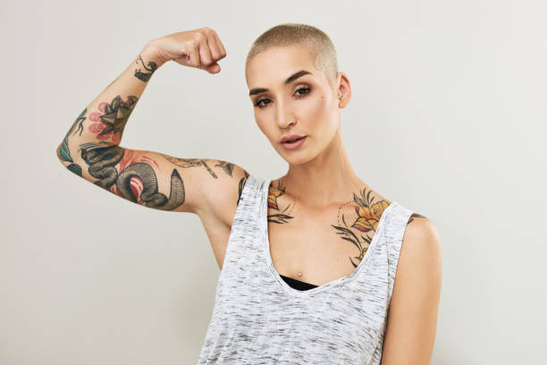 Portrait of an attractive young woman flexing her arm against a grey background Double R, I'm a rebel with a reason tattoo arm stock pictures, royalty-free photos & images