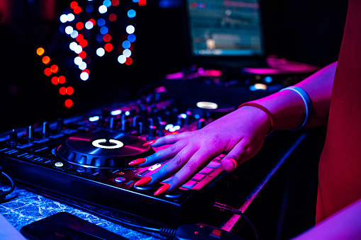 hand of a DJ girl on the background of a music controller mixer at a party in a nightclub
