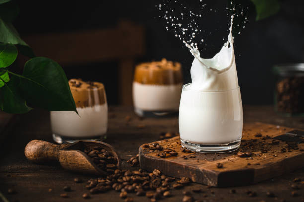 éclaboussure de lait dans un verre avec des grains de café sur la table - milk shake coffee latté cold photos et images de collection