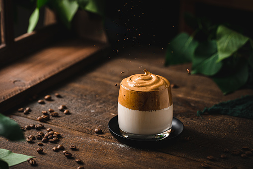 A glass of freshly prepared Dalgona coffee on wooden table. Dalgona frothy coffee made from whipped instant coffee, sugar and milk on table.