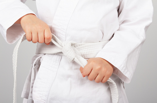 Children's sports. Karate. Children's hands tying a white karate kimono belt