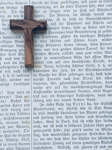 Crucifix lying on a printed text page from 19th century, german language