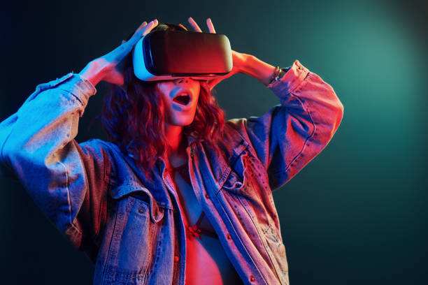 Facial expression of young girl with virtual reality glasses on head in red and blue neon in studio Facial expression of young girl with virtual reality glasses on head in red and blue neon in studio. virtual reality stock pictures, royalty-free photos & images