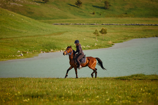 Young woman enjoying horseback riding by the lake