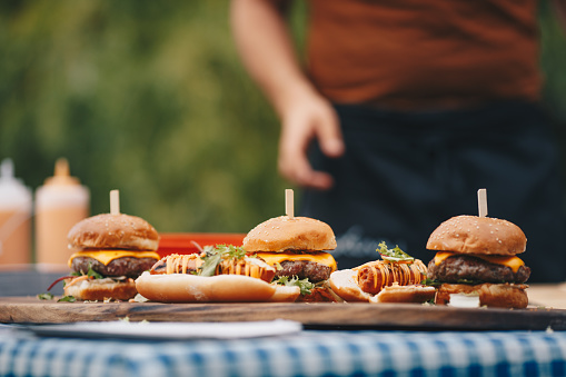 Hot dogs and hamburgers on wooden board. Food on picnic table. Home made barbeque served for lunch outdoors.