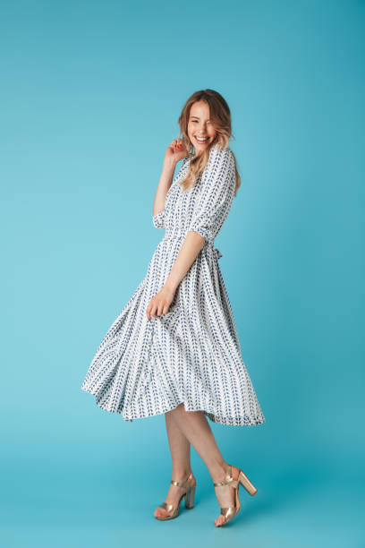 Full length image of Laughing blonde woman in dress dancing Full length image of Laughing blonde woman in dress dancing and looking at the camera over blue background blonde model in dress stock pictures, royalty-free photos & images