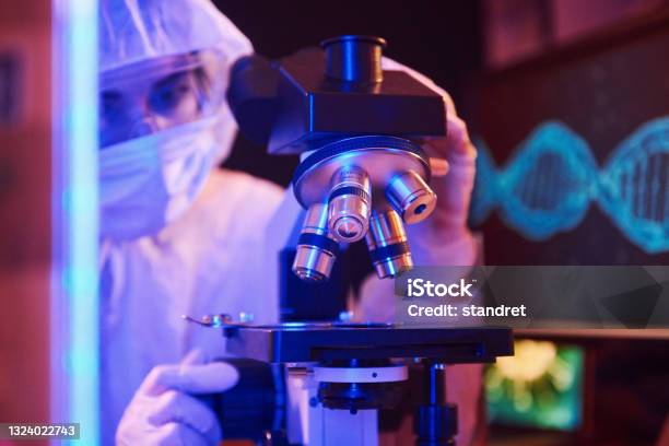 Nurse In Mask And White Uniform Sitting In Neon Lighted Laboratory With Computer Microscope And Medical Equipment Searching For Coronavirus Vaccine Stock Photo - Download Image Now