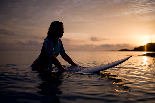 Silhouette of woman on surfboard at sunrise.