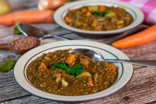 A plate of fresh cooked vegetarian and vegan lentil soup served on a rustic stoneware plate on wooden table background
