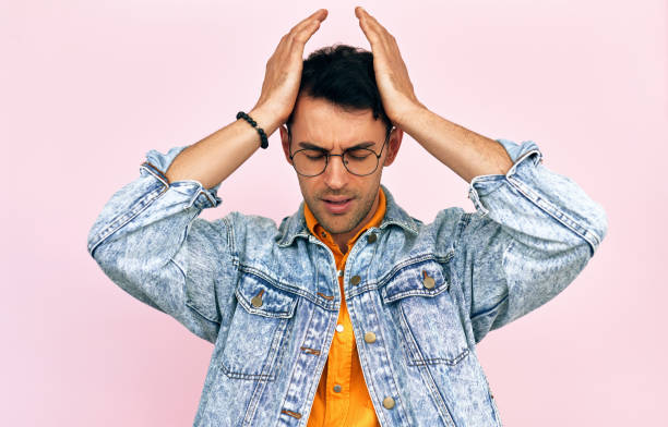 istock Studio image of a frustrated young man dressed in a denim jacket and transparent spectacles keeping both hands on his head isolated on pink background. Confused male feeling sad after making mistake. 1324030986