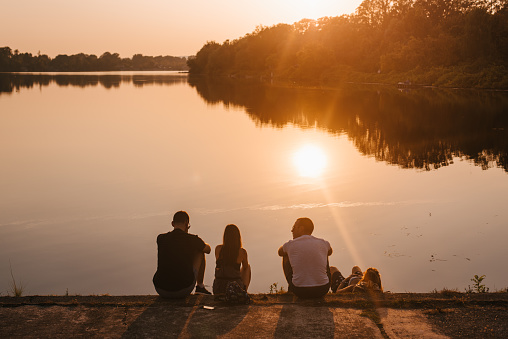 A group of friends sitting on the lakeshore watching the golden sunset over calm lake water