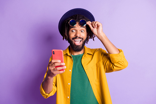 Photo of impressed funny dark skin guy hand touch sunglass look phone like subscribe isolated on violet color background.