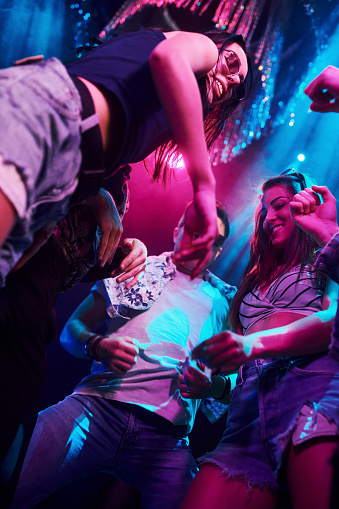 View from below of young people that having fun in night club with colorful laser lights.