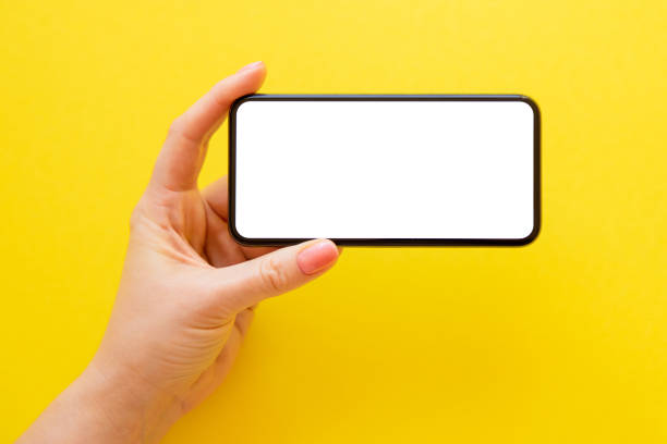 Person holding smart phone with white blank screen in hand on yellow background