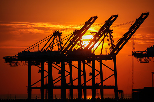 Sunset over cranes in one of the many docks in the Port of Zeebrugge in Belgium. The port is a large container, bulk cargo, new vehicle and passenger ferry terminal handling over 50 million tonnes of cargo annually.