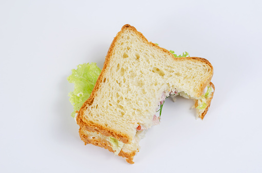 Half-eaten Turkey Sandwich on a white background. Turkey, red tomatoes, green lettuce, dill and white sauce. Food scraps. Top view