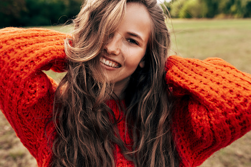 Retrato al aire libre de una joven sonriente con un suéter naranja de punto posando sobre el fondo de la naturaleza. La hermosa hembra tiene una expresión alegre, descansando en el parque. photo