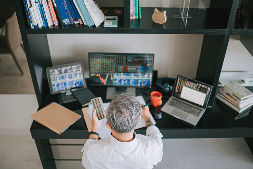 high angle view rear view senior chinese man with hair stubble working at home with stock exchange market multiple computer monitor monitoring market trend