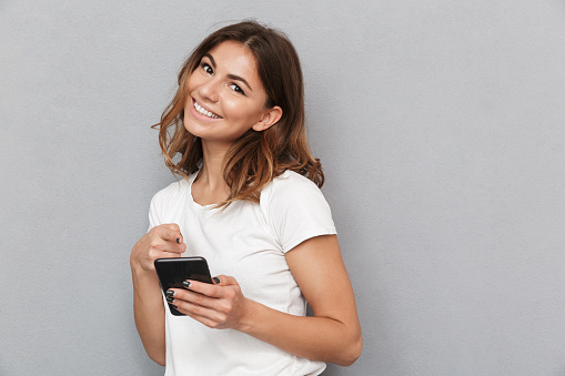 Portrait of a smiling young woman holding mobile phone over gray background
