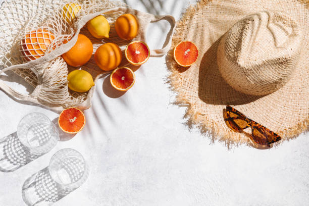 Summer fashion flat lay on white background. Holiday party, vacation, travel, tropical concept. Straw hat, sunglasses, glass and citrus fruits. Palm shadow and sunlight, sun. Top view, copy space. stock photo