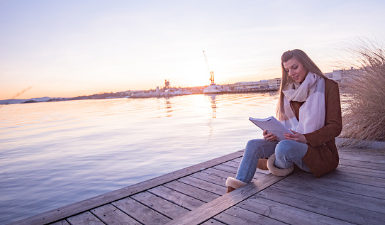 Young female reading a book and sitting on the pier