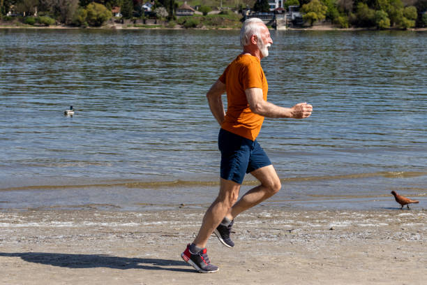 älterer mann joggt am fluss. - beach shorts stock-fotos und bilder