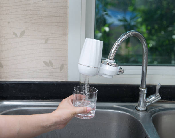 femme versant de l’eau dans le verre du filtre à eau dans la cuisine. - water filter photos et images de collection