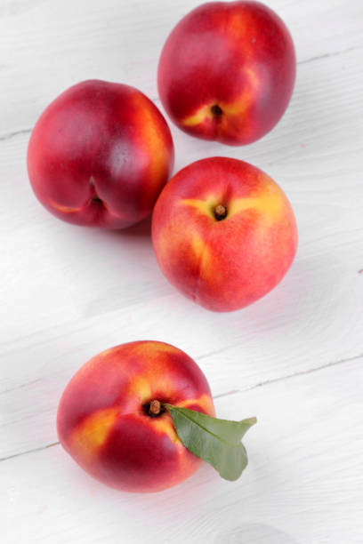 istock Ripe large nectarines with a green leaf close-up on a white wooden background 1324053369