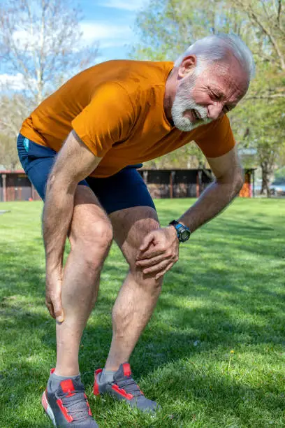 Senior man frowning with muscle pain during training outdoors. Calf leg cramps trauma.