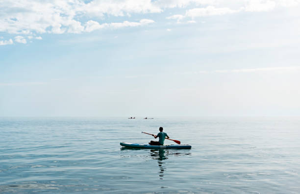 istock Young man from behind on stand up paddle board on the sea on sunny summer day 1324054749
