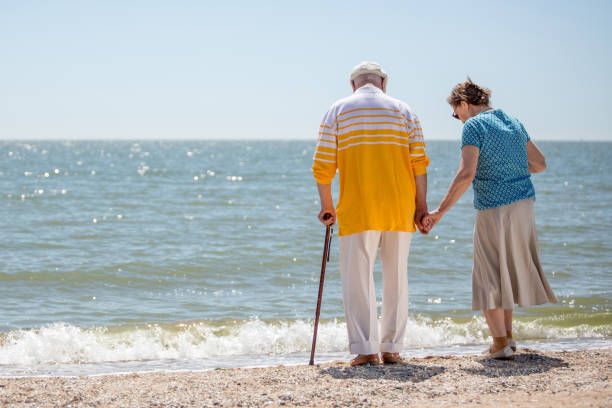 pareja de ancianos caminando a lo largo de la playa juntos - 80 89 años fotografías e imágenes de stock
