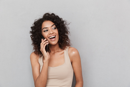 Portrait of a laughing young african woman talking on mobile phone over gray background