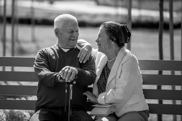 Bondi, NSW, Australia, 10192024: Black and white image of an old lady and man sitting apart on a bench beside a concrete wall and railing