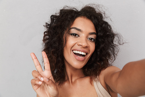 Close up portrait of a happy young african woman taking a selfie with outstretched arm over gray background