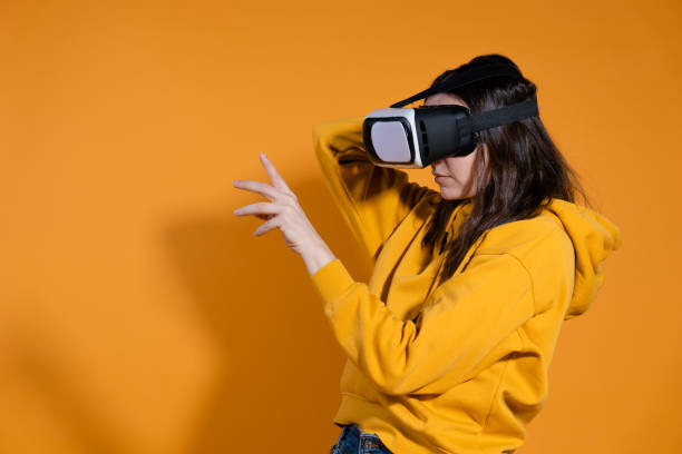 istock young woman with a virtual reality device on a yellow background. 1324056320