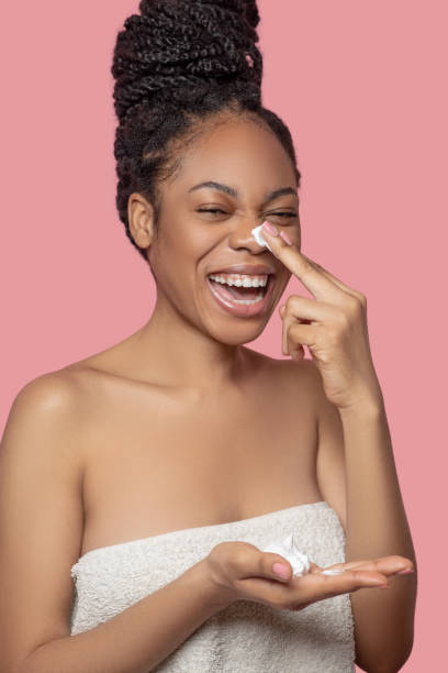 istock Dark-skinned woman applying mositurizer on her face and smiling 1324058985