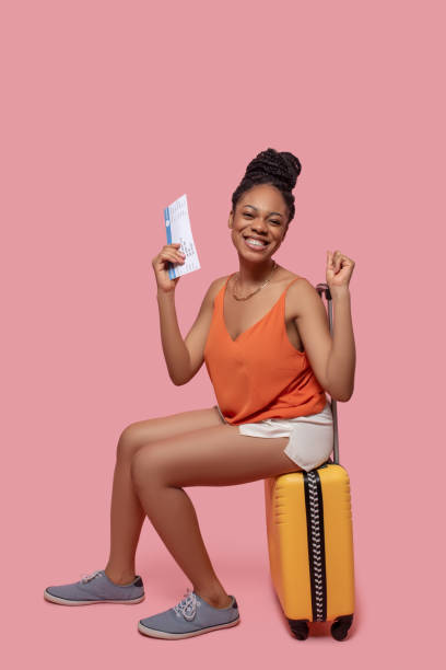 istock Dark-skinned woman holding a suitcase and a plane ticket and looking anticipated 1324059096