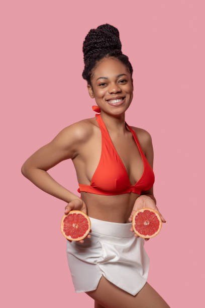 istock Dark-skinned woman holding grapefruit slices and looking happy 1324059225