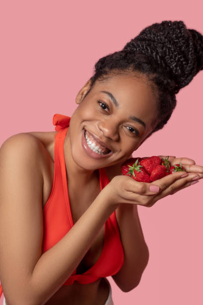istock Mulatta in orange top holding strawberries in her hands 1324059240