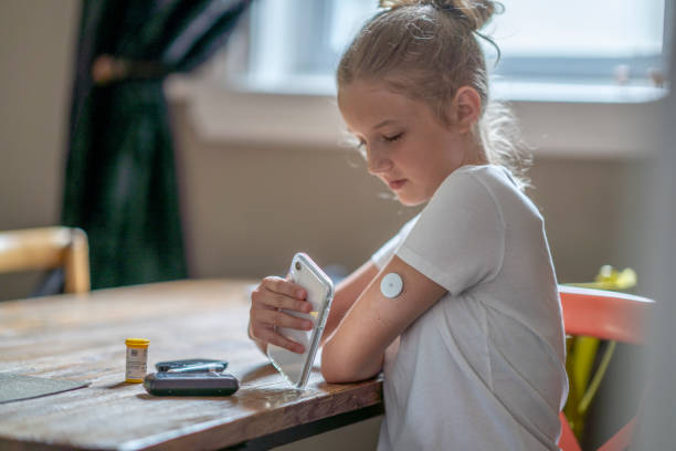 At home diabetes technology A fourteen year old Caucasian girl reads her blood sugar level by placing her cellphone next to her pump in her arm as she sits at a dining table. girl patient stock pictures, royalty-free photos & images