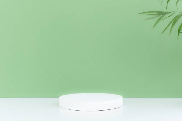 istock Pedestal podium on a white table, green background with palm tree leaves. 1324060858