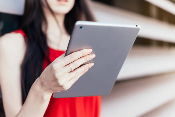 Unrecognizable woman holding a tablet with her hand in red dress. stock photo